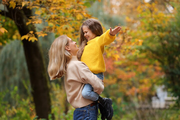 Happy mother with her daughter playing together in autumn park