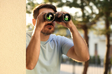 Concept of private life. Curious man with binoculars spying on neighbours outdoors