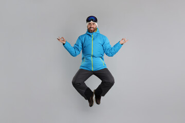 Winter sports. Happy man in ski suit and goggles jumping on gray background