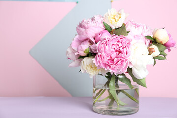 Bouquet of beautiful peonies in vase on lilac table. Space for text