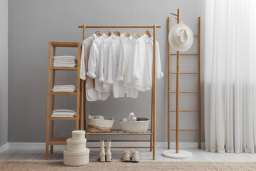 Wardrobe organization. Rack with different stylish clothes, boxes and shelving unit near grey wall...
