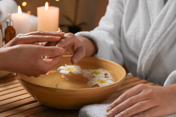 Obraz na płótnie Canvas Woman receiving hand massage in spa salon, closeup. Bowl of water and flowers on wooden table