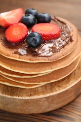Tasty pancakes with chocolate paste and berries on wooden table, closeup