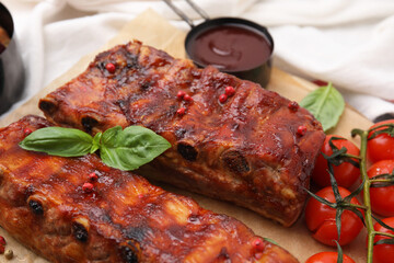 Tasty roasted pork ribs served with sauce, basil and tomatoes on table, closeup