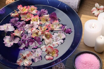 Bowl of water with flowers, sea salt and candles on table. Spa treatment