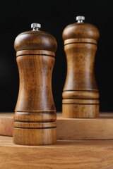 Salt and pepper shakers on wooden table against black background, closeup