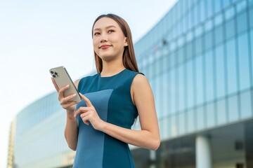 Asian Businesswoman Using Smartphone In Front a Modern Office Building in Central Business District