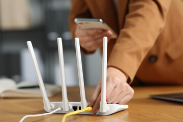 Woman with smartphone connecting cable to Wi-Fi router at table indoors, closeup