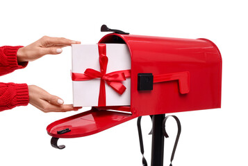 Woman putting Christmas gift into mailbox on white background, closeup. Sending present by mail