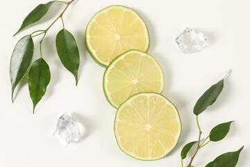 Lime pieces, ice and green leaves on white background, flat lay