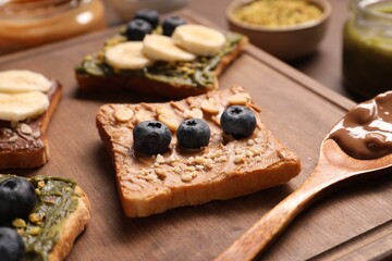 Toasts with different nut butters, banana slices, blueberries and nuts on wooden board, closeup