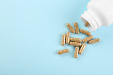 Bottle and vitamin capsules on light blue background, top view. Space for text