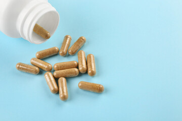 Bottle and vitamin capsules on light blue background, closeup. Space for text