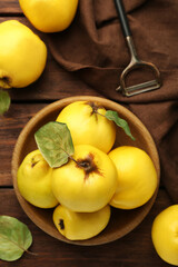 Tasty ripe quince fruits in bowl and peeler on wooden table, flat lay
