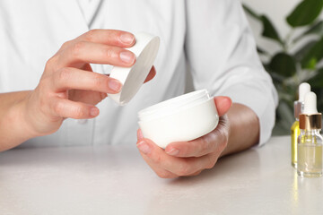Fototapeta na wymiar Dermatologist holding jar of cream at white table, closeup. Developing cosmetic product