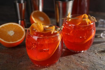 Aperol spritz cocktail, ice cubes and orange slices in glasses on grey textured table, closeup