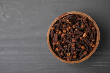 Aromatic cloves in bowl on grey wooden table, top view. Space for text
