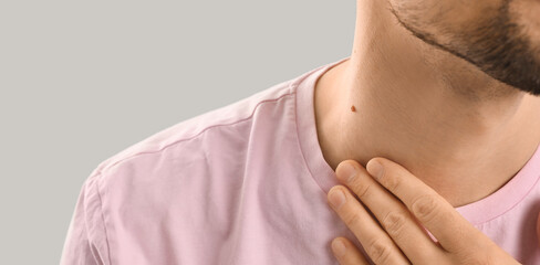 Man with mole on neck against grey background, closeup