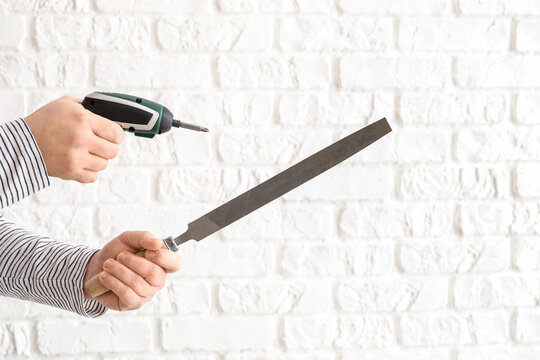 Worker with screwdriver and file on white brick background