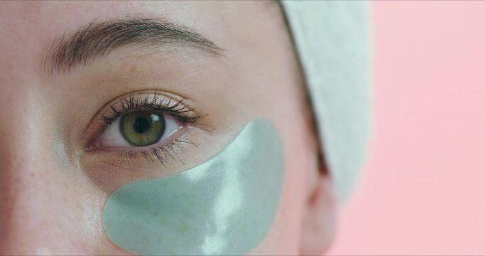 Closeup of eye, patch and facial for beauty, wellness and cosmetics isolated on pink background. Dermatology, gel mask product for skincare and healthy skin in studio with microblading and eyelash