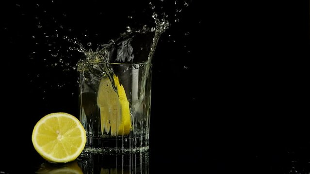 A slice of lemon falls into a glass of water. Slow motion. Isolated on black background.