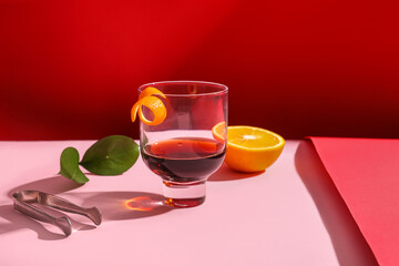 Glass of rum with orange and ice tongs on colorful background