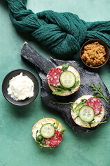 Board with tasty sandwiches, mustard and cream cheese on color background