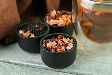 Bowls with different dried fruit tea on green wooden table, closeup