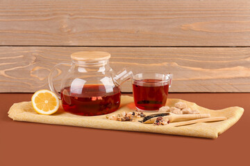 Teapot and glass of fruit tea on brown table near wooden wall