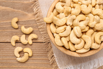 Bowl with tasty cashew nuts on wooden background