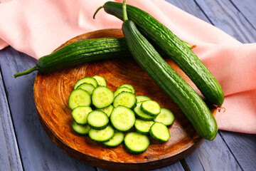 Plate with cut and whole cucumbers on grey wooden background
