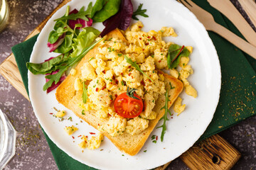 Plate with tasty scrambled eggs sandwich and salad on grey background