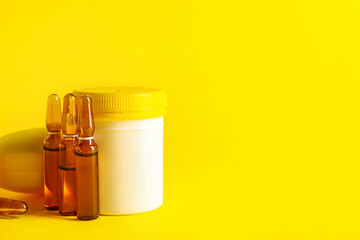 Ampules and jar with pills on yellow background