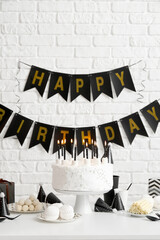 Birthday cake with candles on white table and garlands on brick wall