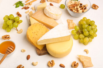 Board with different types of tasty cheese and grapes on light background