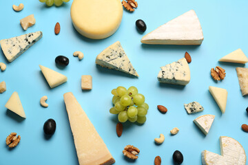 Different types of tasty cheese, nuts and grapes on blue background