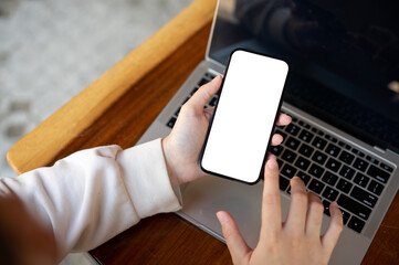 Top view image of a woman using her smartphone at her working desk. A white-screen smartphone mockup