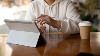 A female college student or a freelancer is using her digital tablet while sitting in a coffee shop.