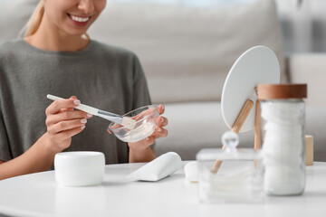 Young woman preparing face mask in front of mirror at home, closeup. Spa treatments