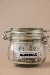 Saving Money In Glass Jar filled with Dollars banknotes. INSURANCE transcription in front of jar. Managing personal finances extra income for future insecurity. Beige background