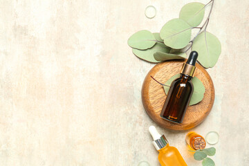 Cosmetic oil bottles with wooden stand and eucalyptus branch on textured background