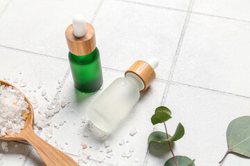 Cosmetic oil bottles with wooden spoon, eucalyptus branch and sea salt on tile background