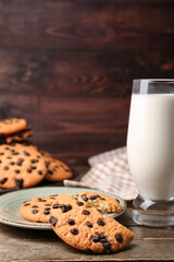 Glass of milk and tasty cookies with chocolate chips on wooden background