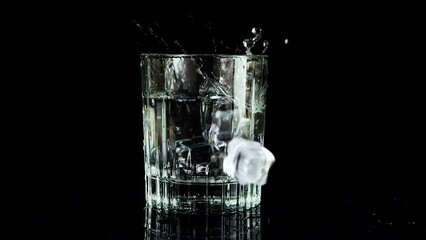 Ice cubes falling into a glass of water on a black background. Slow motion. - Powered by Adobe