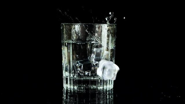 Ice cubes falling into a glass of water on a black background. Slow motion.