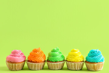 Tasty colorful cupcakes on green background