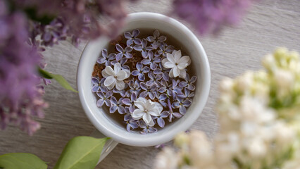Tasty black tea in white cup on windowsill with aromatic lilac flowers. Spring composition Cup of...