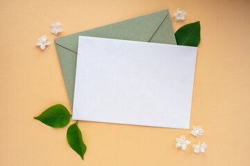 Composition with empty envelope and beautiful spring lilac flowers on beige background. Mockup card invitation greeting card postcard copy space template blank. Branches of lilac blooming bouquet. 
