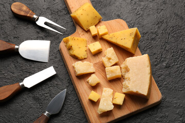 Wooden board with pieces of tasty cheese on dark background