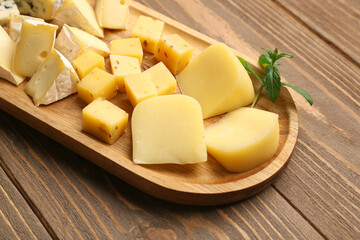 Board with pieces of tasty cheese on wooden background, closeup
